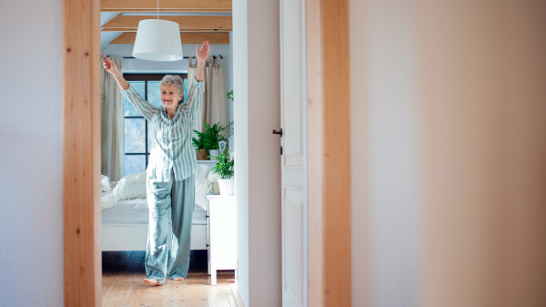 Happy senior woman in bed at home getting up in the morning, stretching.