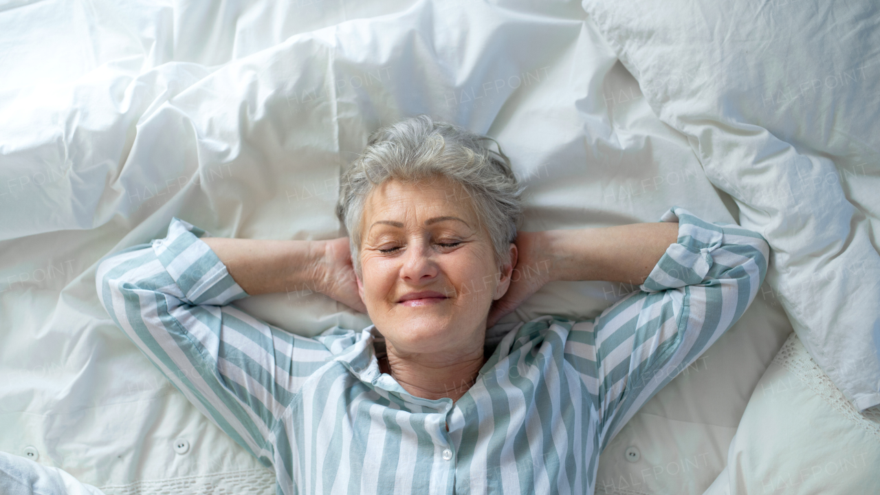 A top view of happy senior woman in bed at home, eyes closed.