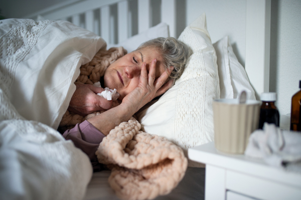 A sick senior woman sleeping in bed at home, cold and flu concept.