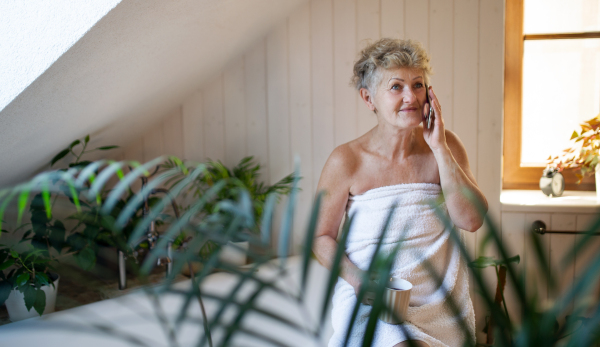 Happy senior woman wrapped in a towel in bathroom at home, sitting and resting with tea.