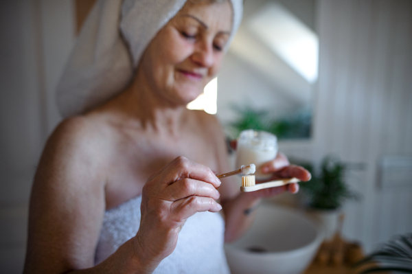 A senior woman in bathroom brushing teeth at home, ecologic and sustainable lifestyle concept.