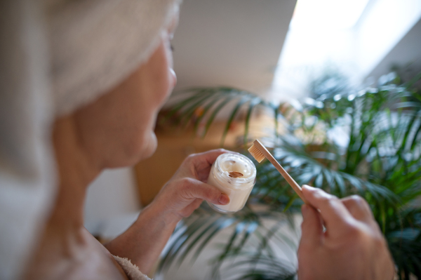 Unrecognizable senior woman in bathroom brushing teeth at home, ecologic and sustainable lifestyle concept.