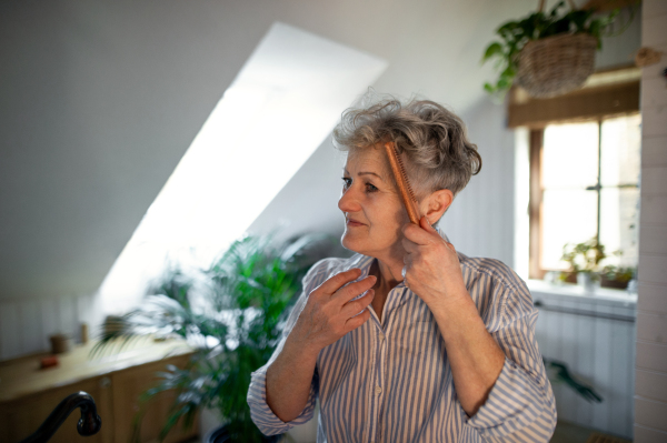 A senior woman in bathroom combing hair at home, ecologic and sustainable lifestyle.