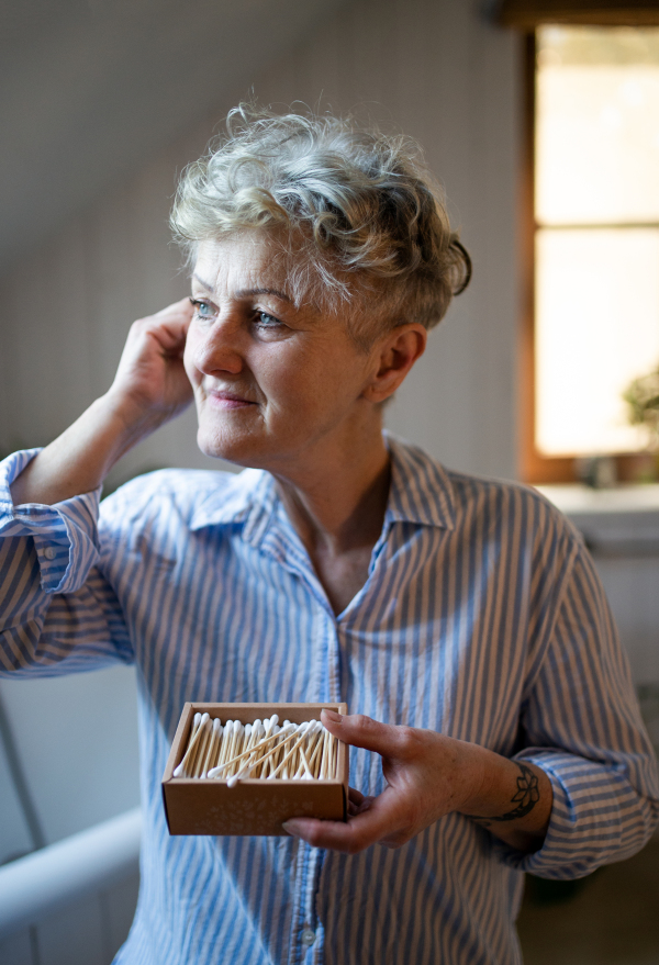 Portrait of senior woman in bathroom using ear cleaning sticks at home, ecologic and sustainable lifestyle.