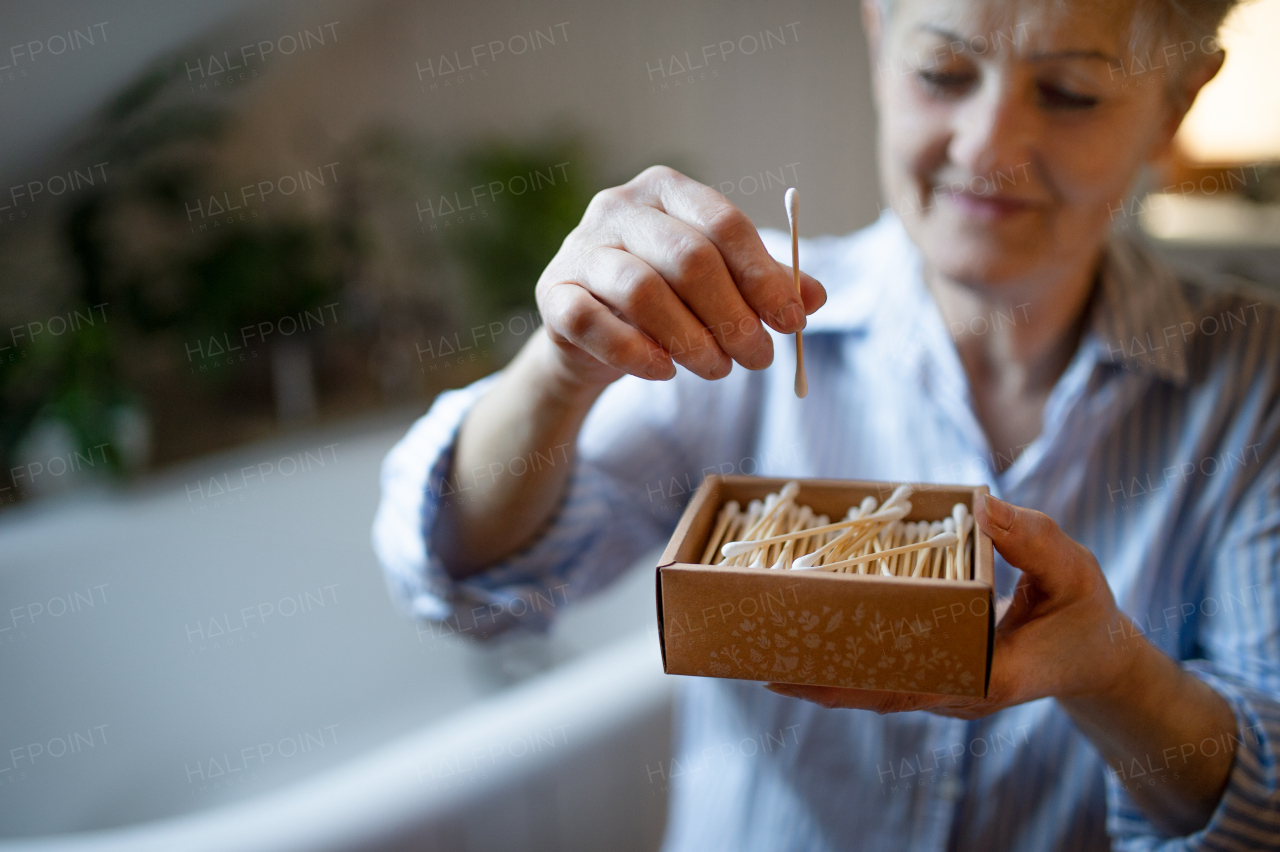 Portrait of senior woman in bathroom using ear cleaning sticks at home, ecologic and sustainable lifestyle.