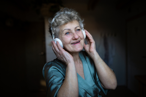 A happy senior woman with headphones listening to music at home, relax and self-care concept.