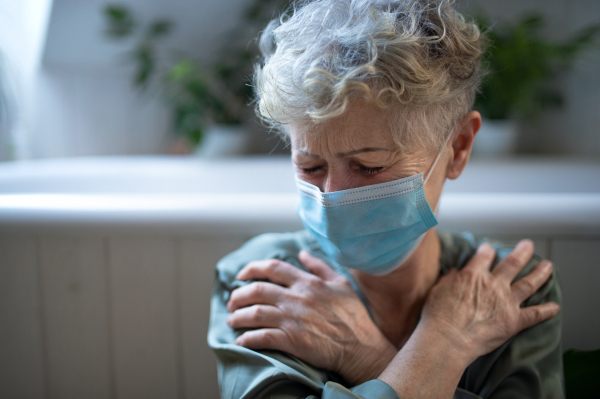 Depressed senior woman with face mask sitting in bathroom at home, coronavirus and mental health concept.