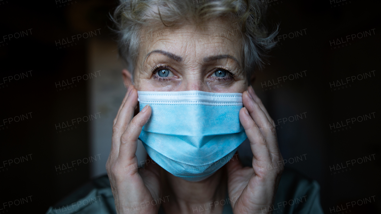 Depressed senior woman with face mask standing in bathroom at home, coronavirus and mental health concept.