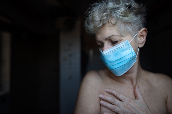 Depressed senior woman with face mask standing in bathroom at home, coronavirus and mental health concept.