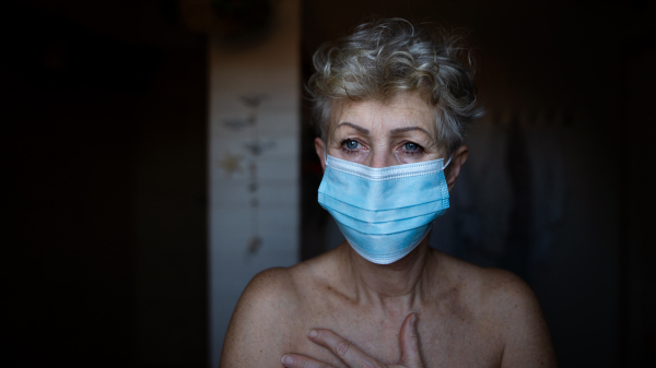 Depressed senior woman with face mask standing in bathroom at home, coronavirus and mental health concept.