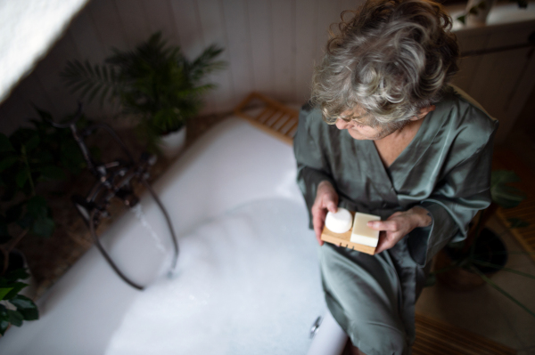 A top view of senior woman in bathroom preparing for a bath at home, ecologic and sustainable lifestyle.