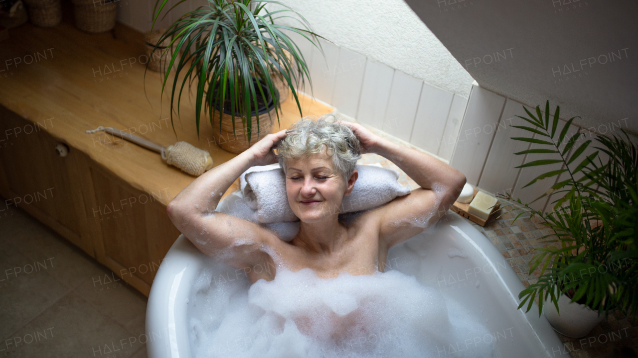 A top view of contented senior woman lying in bath tub at home, eyes closed.