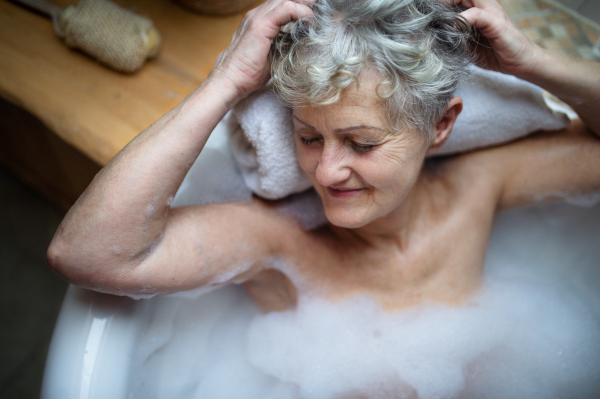 A top view of contented senior woman lying in bath tub at home, eyes closed.