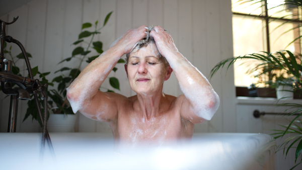 Portrait of contented senior woman washing in bubble bath tub at home, eyes closed.