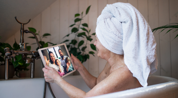 Happy senior woman with tablet in bath tub at home, video call with daughter and grandchildren.