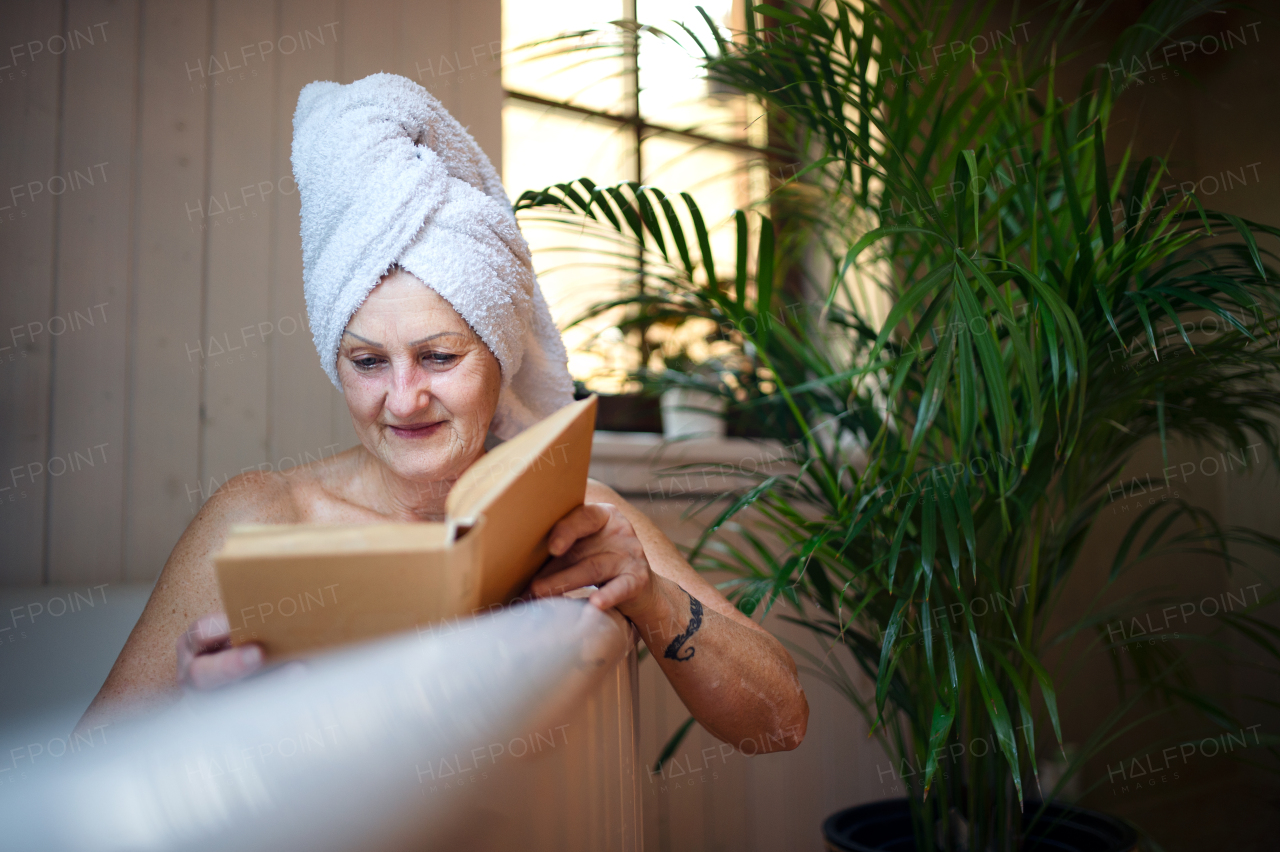 A happy senior woman reading book in bath tub at home.