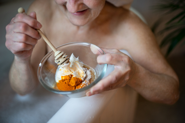 An unrecognizable senior woman relaxing in bath tub at home, preparing beauty face mask.