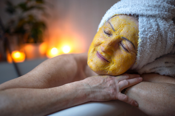 Happy senior woman with beauty face mask in bath tub at home, relaxing with eyes closed.