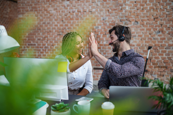 Cheerful young businesspeople sitting and working at desk in office, a cooperation concept.