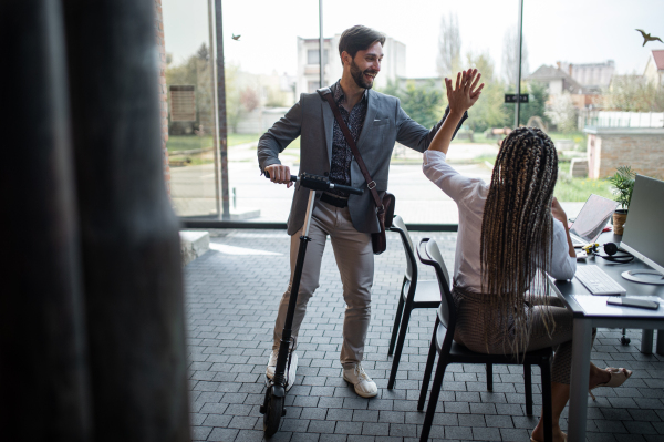 Young businessman with scooter greeting colleague in office, coworking and eco commuting concept.