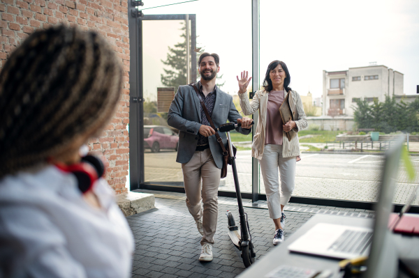 Young and old businesspeople with scooter entering an office, coworking and eco commuting concept.