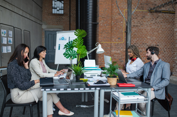 Young and old businesspeople sitting and working at desk in office, a cooperation and coworking concept.