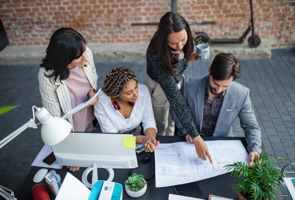 A top view of young and old architects sitting and working at desk in office, cooperation concept.