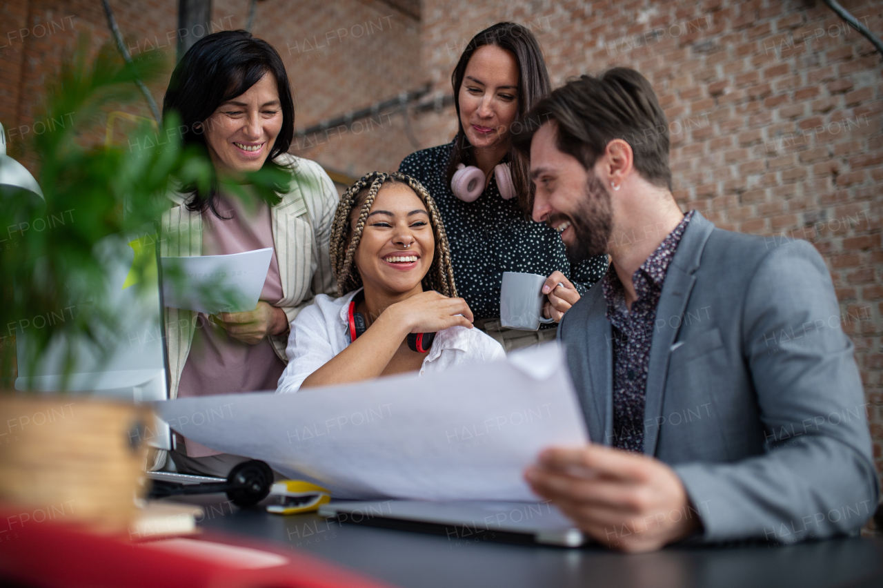 Cheerful young and old businesspeople sitting and working at desk in office, a cooperation concept.