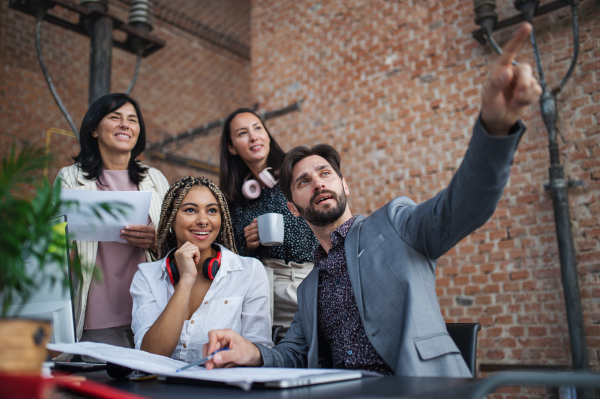 Cheerful young and old businesspeople sitting and working at desk in office, a cooperation concept.