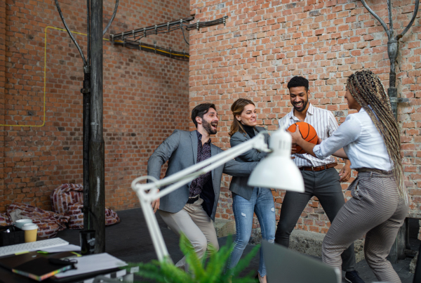 A group of cheerful young businesspeople playing basketball in office, taking a break concept.