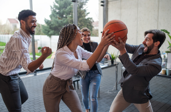 A group of cheerful young businesspeople playing basketball in office, taking a break concept.