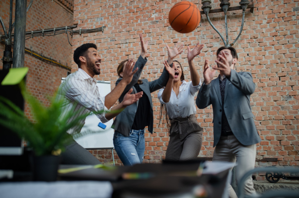 A group of cheerful young businesspeople playing basketball in office, taking a break concept.