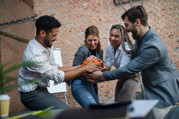 A group of cheerful young businesspeople playing basketball in office, taking a break concept.