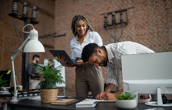 Cheerful young businesspeople with laptop working in office, a cooperation concept.