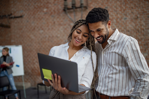 Cheerful young businesspeople with laptop working in office, a cooperation concept.