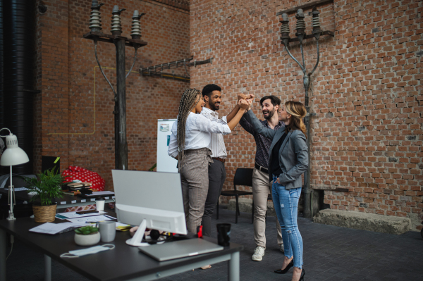 Cheerful young businesspeople standing in an office, cooperation and celebrating new contract concept.