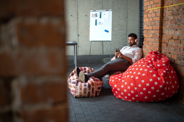 Young businessman with smartphone and headphones taking a break in an office, resting.