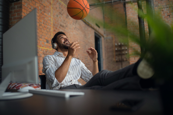 A cheerful young businessman with headphones and ball taking a break in office, resting.