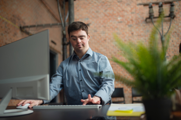 Cheerful young Down Syndrome businessman working at desk in anoffice, social inclusion concept.