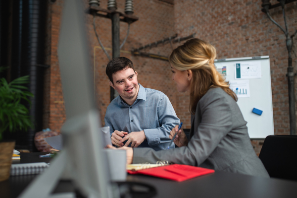 A happy down syndrome man with businesswoman colleague working in office, social inclusion and cooperation concept.