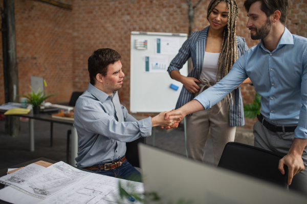 A down syndrome man shaking hands with businesspeople in office, social inclusion and cooperation concept.