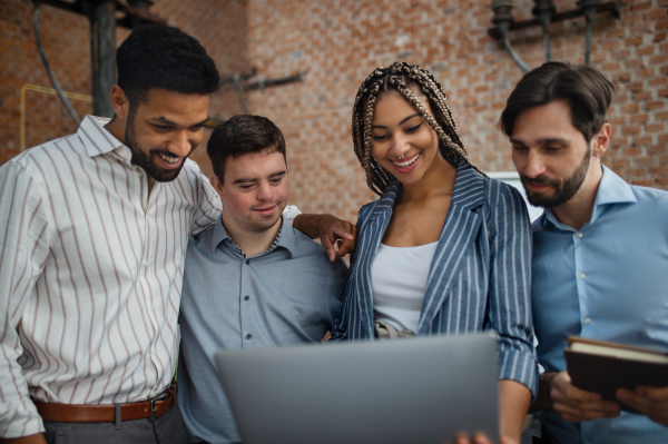 Cheerful young businesspeople with laptop working in office, social inclusion and a cooperation concept.