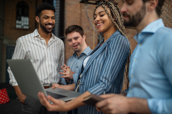 Cheerful young businesspeople with laptop working in office, social inclusion and a cooperation concept.