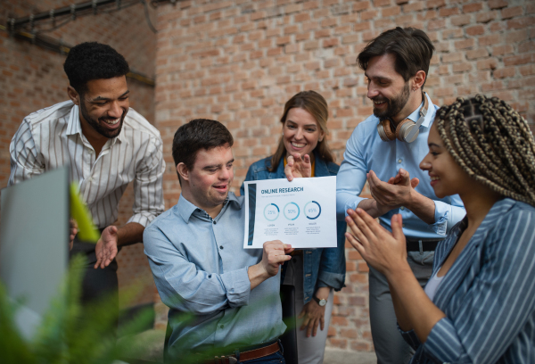 A happy down syndrome man with business colleagues in office, social inclusion and cooperation concept.