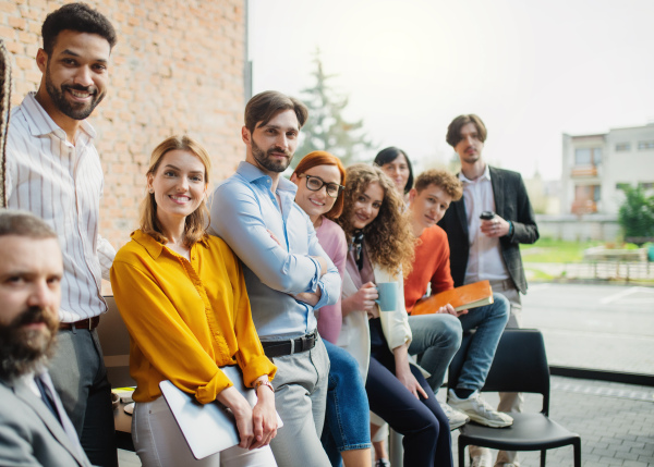 A portrait of young businessman with group of entrepreneurs indoors in office, looking at camera.