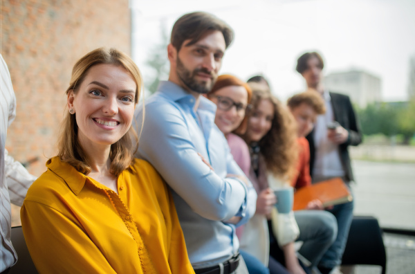 A portrait of young businesswoman with group of entrepreneurs indoors in office, looking at camera.