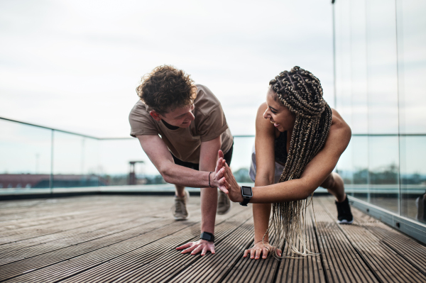 Happy young couple doing exercise outdoors on terrace, sport and healthy lifestyle concept.