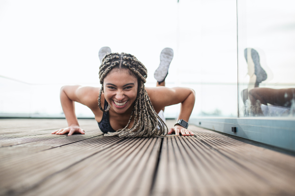 A young woman doing exercise and looking at camera outdoors on terrace, sport and healthy lifestyle concept.