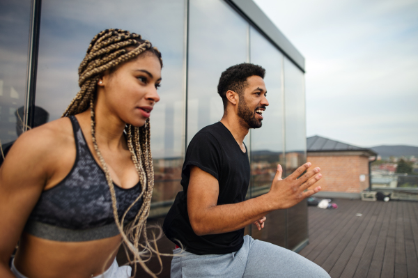 A side view of young couple doing warm up exercise outdoors on terrace, sport and healthy lifestyle concept.