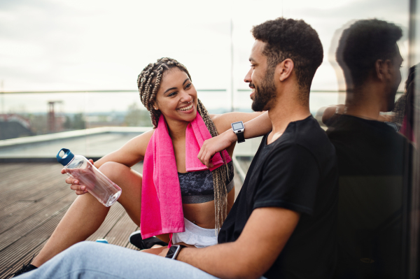 A young couple resting after exercise outdoors on terrace, sport and healthy lifestyle concept.